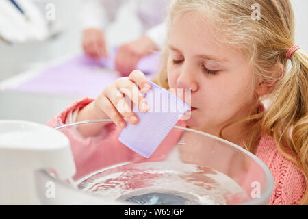 Kleines Mädchen als Patient spült den Mund mit Wasser, während vom Zahnarzt behandelt werden Stockfoto