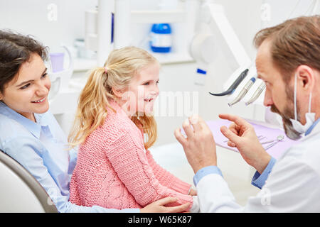 Pädiatrische Zahnarzt erklärt die Mutter und das Kind die Behandlung in der Konsultation in der Arztpraxis Stockfoto