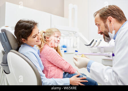 Pädiatrische Zahnarzt erklärt Kind auf dem Schoß der Mutter die geplante Behandlung in der Arztpraxis Stockfoto