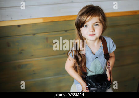 Closeup Bild eines kleinen niedliche Mädchen mit langen Haaren auf einem Stuhl sitzend, holding Foto Kamera. Stockfoto