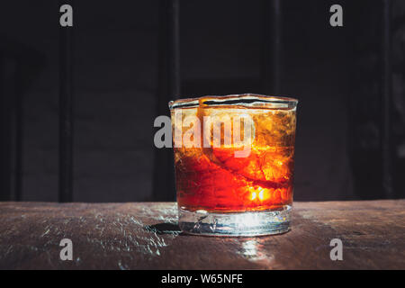 Risse whisky Glas. Alkohol Cocktail mit schönen Hintergrundbeleuchtung auf einem Holztisch. Mit Eis und Orangenschale serviert. Boulvardier oder Negroni. Stockfoto
