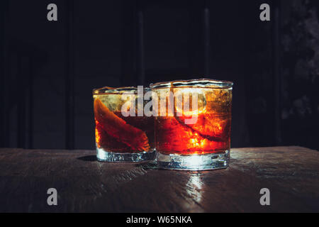 Zwei gebrochene Whisky Gläser. Alkohol Cocktails mit schönen Hintergrundbeleuchtung auf einem Holztisch. Mit Eis und Orangenschale serviert. Boulvardier oder Negroni. Stockfoto