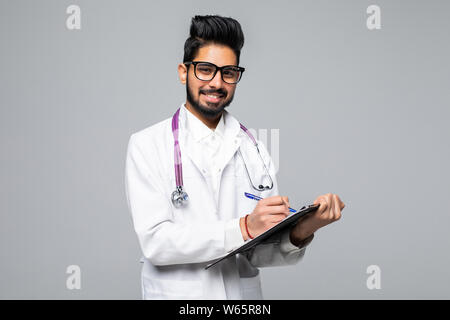Fröhlicher junger männlicher Arzt mit Stethoskop über Hals holding Zwischenablage isoliert auf weißem Stockfoto