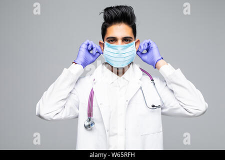 Porträt einer stattlichen Bart Arzt in Scrubs mit Stethoskop und Maske stehen selbstbewusst, auf weißem Hintergrund Stockfoto