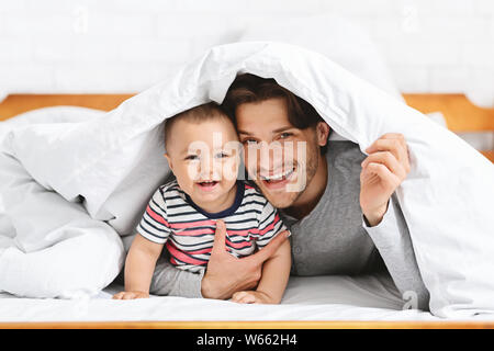 Fröhliches baby versteckt unter Decke mit Vater Stockfoto