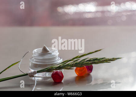 Glas mit weisser Creme und ährchen auf farbigem Glas Kieselsteinen. Ährchen mit weißen Seil gebunden. Auf der Rückseite verschwommenen Hintergrund Blendung. Selektive konzentrieren. Pl Stockfoto