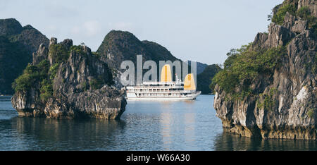 Touristische Kreuzfahrtschiffe Segeln unter Kalkstein Berge in der Halong Bay, Vietnam. Rahmung mit Baum Blätter. Stockfoto