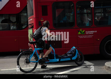 Frau auf einem Fahrrad mit einer Verlängerung auf der Vorderseite versucht durch die geschäftigen Londoner Verkehr im Juli zu manövrieren. Stockfoto