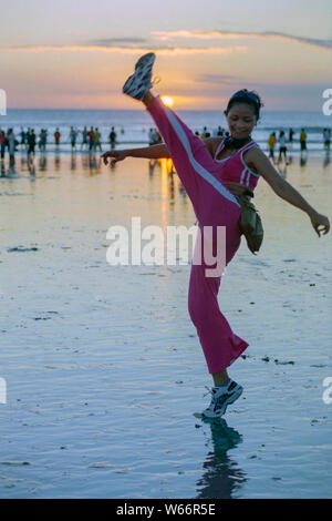 Eine junge indonesische Frau in Sportkleidung, die an einem belebten Strand von kuta bei Sonnenuntergang bali indonesia ihre „Keep fit“-Routine durchläuft Stockfoto