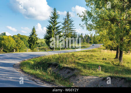 Alte Serpentinenstraße bergauf durch den Wald. schönen abend Transport Landschaft. Fluffy Clouds auf dem azurblauen Himmel. Risse im Asphalt und Schotter roadsi Stockfoto