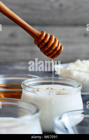 Gegorene Getränk Kefir in kleinen Flaschen und Honig auf grauem Hintergrund Nahaufnahme Stockfoto