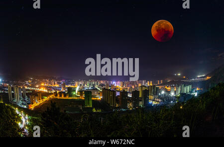 Blick auf den längsten 'Blood Moon' Sonnenfinsternis dieses Jahrhunderts, die in den Schatten der Erde vergeht, im Himmel über die Wolkenkratzer bei einer totalen Mondfinsternis e Stockfoto