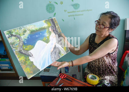 Die Mutter der 40-jährige Chinesin Zhang Junli, die gelähmt, seit sie acht war, bereitet ein Ölgemälde erstellt von Zhang zu Paket Stockfoto