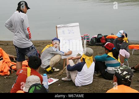 Eine Gruppe junger Erwachsener versammelt sich neben einem Wasserdamm und diskutiert über ihren Aktivierungsplan im Freien auf einem weißen Brett. Stockfoto