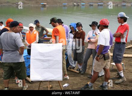 Eine Gruppe junger Erwachsener versammelt sich neben einem Wasserdamm und diskutiert über ihren Aktivierungsplan im Freien auf einem weißen Brett. Stockfoto