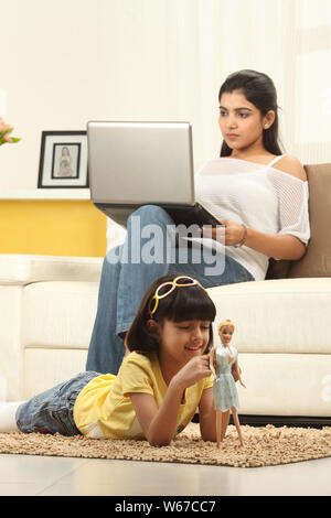 Mädchen spielen auf dem Boden mit Mutter mit Laptop auf Couch Stockfoto