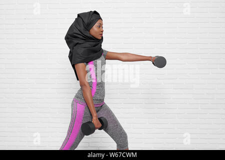 Ansicht von der Seite der muslimischen Frau im Sport einheitliche Sport auf weißem Hintergrund isoliert. Junge religiöse Frauen in Schwarz hijab halten Kurzhanteln und Fitness. Konzept der Muskeln und der Gesundheit. Stockfoto