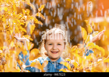 Porträt eines niedlichen kleinen Mädchen stehen im Herbst Park im Regen. Das Kind streckte seine Hände und sammelt die Tropfen in seiner Handfläche. Stockfoto