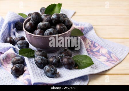 Keramische Schüssel mit frischen Pflaumen und Blau rustikal Serviette auf die weiße Holztisch Stockfoto