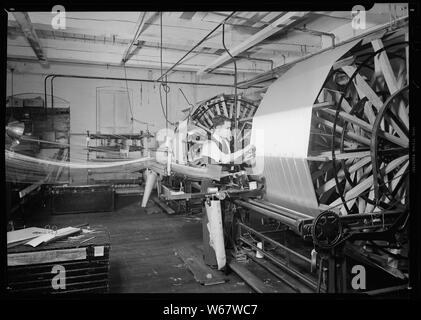 Paterson, New Jersey - Textilien. Die kettfäden der Abschnitt, der nur auf dem Rahmen Wunde wurde abgebaut worden; Umfang und Inhalt: Paterson, New Jersey - Textilien. Die kettfäden der Abschnitt, der nur auf dem Rahmen Wunde wurde abgebaut worden. Der Bediener wird angezeigt, bis die Enden der Abschnitt. Die gebundene Enden der Abschnitte zuvor Wunde sind deutlich sichtbar auf dem Rahmen, alle in Uniform. Sobald dieser Operator beendet ist, wird der neue Abschnitt wird gestartet. Die Anzahl der Threads in einem Abschnitt wird durch die Anzahl der Spulen auf den creel bestimmt. Mit der Art Stockfoto