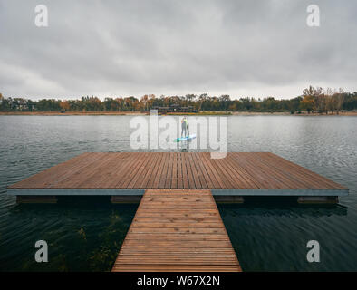 Athlet im Neoprenanzug auf paddleboard Erkundung der See bei kaltem Wetter gegen bewölkten Himmel Stockfoto