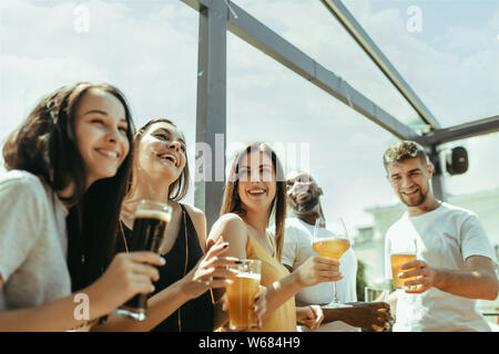 Junge Gruppe von Freunden Bier trinken, Spaß haben und Feiern gemeinsam Laughting. Frauen und Männer mit Brille's Bier in sonniger Tag. Oktoberfest, Freundschaft, Gemeinsamkeit, Glück, Sommer Konzept. Stockfoto