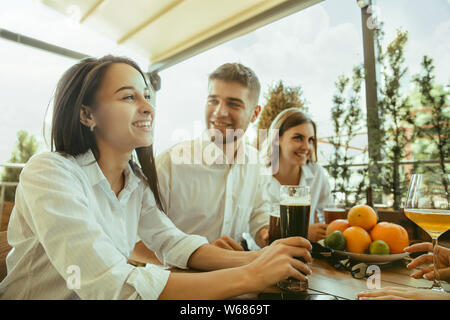 Junge Gruppe von Freunden Bier trinken, Spaß haben und Feiern gemeinsam Laughting. Frauen und Männer mit Brille's Bier in sonniger Tag. Oktoberfest, Freundschaft, Gemeinsamkeit, Glück, Sommer Konzept. Stockfoto