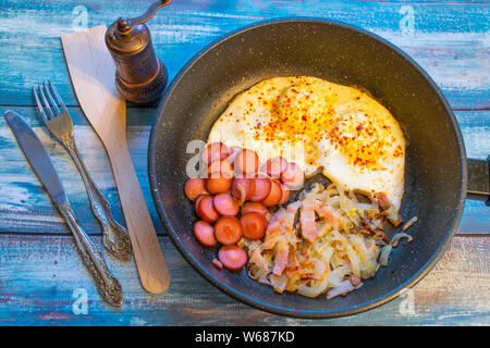 Rührei mit Speck, Zwiebeln und Würstchen. In der Pfanne auf den Tisch. Stockfoto