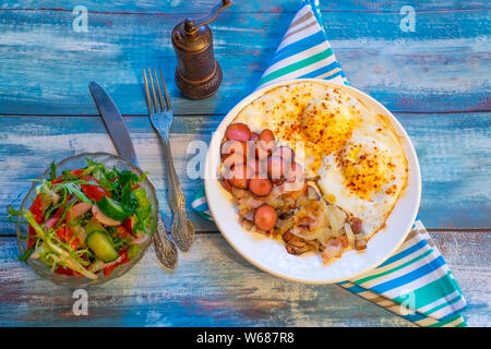 Rührei mit Speck, Zwiebeln und Würstchen. Auf einem Teller auf den Tisch. Stockfoto