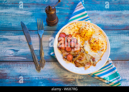 Rührei mit Speck, Zwiebeln und Würstchen. Auf einem Teller auf den Tisch. Stockfoto