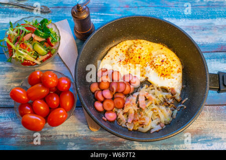 Rührei mit Speck, Zwiebeln und Würstchen. In der Pfanne auf den Tisch. Stockfoto