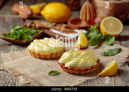 Törtchen mit Zitronencreme und Minze auf einen alten Holztisch. Hausgemachte Desserts mit Zutaten und Küchengeräte aus Holz. Stockfoto