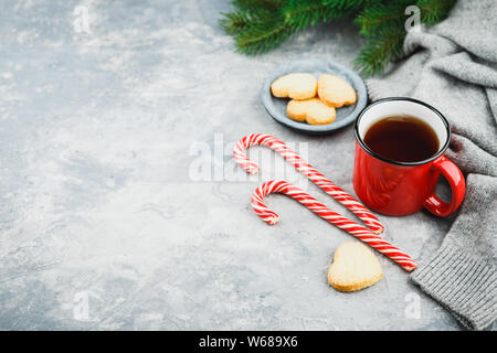 Weihnachten rot emailliert Tasse Tee, Keksen Sugar Cookies in Form von Herzen, die Zweige der Fichte und Zuckerstangen auf einem hellen Hintergrund. Raum fo Stockfoto