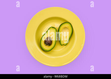 Slice avocado Obst. Schüssel mit Gelb und Avocado auf einem violetten Hintergrund. Nützliche Ernährung Lebensmittel mit Vitaminen. Das Konzept der Verwendung in der Medizin Stockfoto