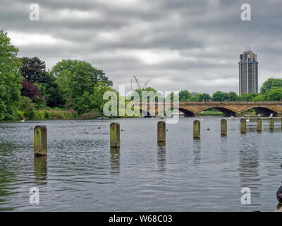 Die lange Wasser in Kensington Gardens, einer städtischen Grünfläche in London, die zu den Sepentine Bridge und die Skyline der Stadt in der Ferne Stockfoto