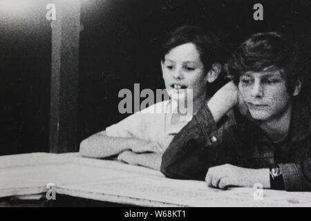 Feine schwarze und weiße Kunst Fotografie aus einem Bündel von Happy lucky school Jungen an einem Tisch sitzen aus den 1970er Jahren gehen. Stockfoto