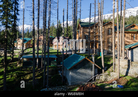 Tagsüber Aussicht auf die schneebedeckten Pir Panjal Reihe über Häuser und Hotels inmitten von Pinien in Gulmarg, Jammu und Kaschmir, Indien Stockfoto