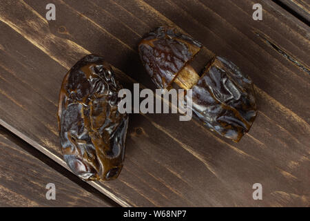 Gruppe von einer ganzen zwei Hälften von getrockneten braunen Datum Medjool flatlay auf braunem Holz Stockfoto