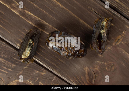 Gruppe von einer ganzen zwei Hälften von getrockneten braunen Datum Medjool flatlay auf braunem Holz Stockfoto