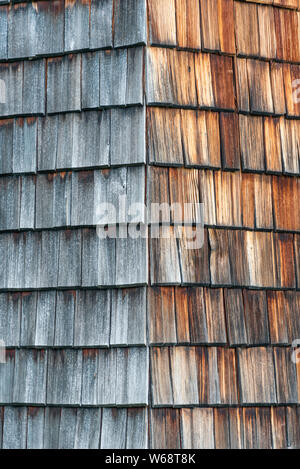 Verwittert und von der Sonne verblasst Holzschindeln, die Fassade eines Alpine House. Holz Textur in den Farben Grau und Orange. Stockfoto