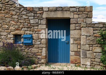 Äußere Detail in einem Ferienhaus aus Stein mit blauer Farbe Tür und kleinen blauen Fenster. Kleiner Garten mit Lavendel. Stockfoto