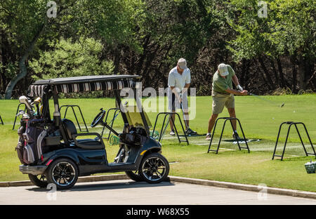 Zwei ältere Männer, die Golf üben, das auf einer Praxisstrecke auf einem Sun City, Texas Erwachsenen-Ruhestand-Gemeinschaftsgolfkurs fährt Stockfoto