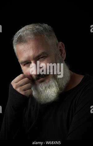 Portrait von lächelnden brutale grauhaariger Mann mit ein grauhaariger üppigen Bart auf einem schwarzen Hintergrund, selektiver Fokus Stockfoto