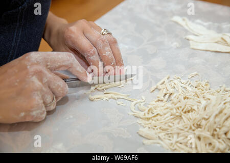 Junge Haus Frau Vorbereiten der hausgemachte Pasta in der Küche. Teig schneiden lange Streifen für Kochen Pasta. Hausgemachte Speisen Vorbereitung Konzept. Nahaufnahme des p Stockfoto
