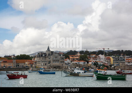 Verschiedene farbige Boote in der Bucht von Cascais, Portugal mit der Uferlinie und Zentrum Gebäude der Altstadt im Hintergrund verankert. Stockfoto