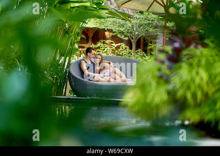 Candid shot der jungen kaukasischen Paar Lounging in modernen Stuhl in der Nähe des luxuriösen Pool von Tropical Hotel und Spa in Bali. Stockfoto