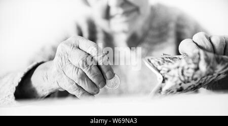 Nahaufnahme der unkenntlich Ältere womans Hände zählen restlichen Münzen von der Pension in Ihrem Portemonnaie nach dem Bezahlen von Rechnungen aufgeführt. Schwarz und Weiß Stockfoto