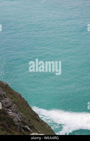 Patch von Gischt Meer Schaum auf eine ruhige türkisfarbene Meer von St Agnes Head, North Cornwall. Marine, UK. Stockfoto