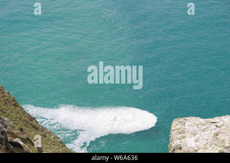 Patch von Gischt Meer Schaum auf eine ruhige türkisfarbene Meer von St Agnes Head, North Cornwall. Marine, UK. Stockfoto