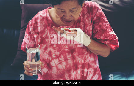 Senior asiatische Frau Pille nehmen Medizin auf der Hand beim Sitzen auf dem Sofa zu Hause Stockfoto